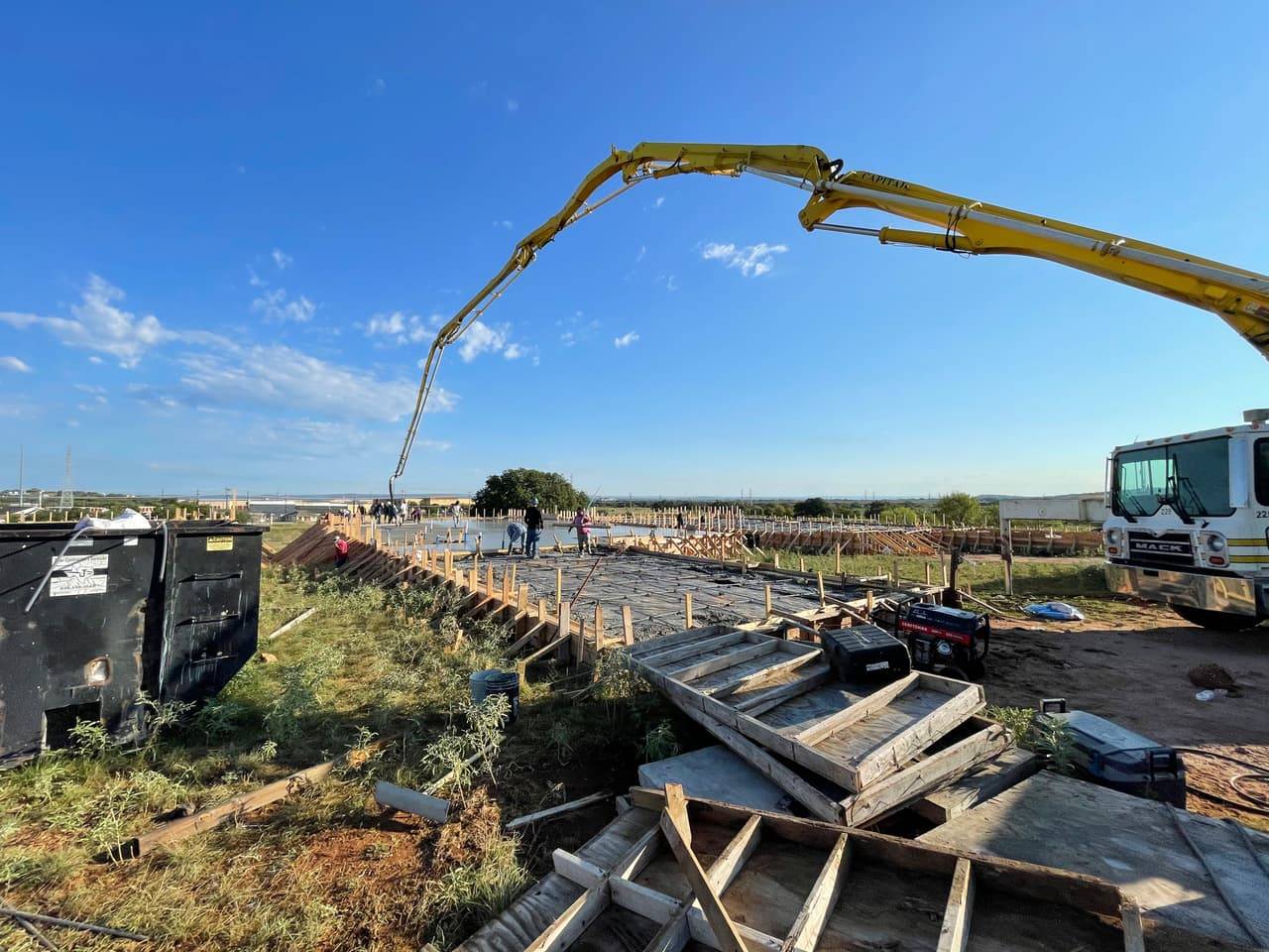 Crew pouring a reinforced concrete slab in a backyard near an in-ground pool with a slide