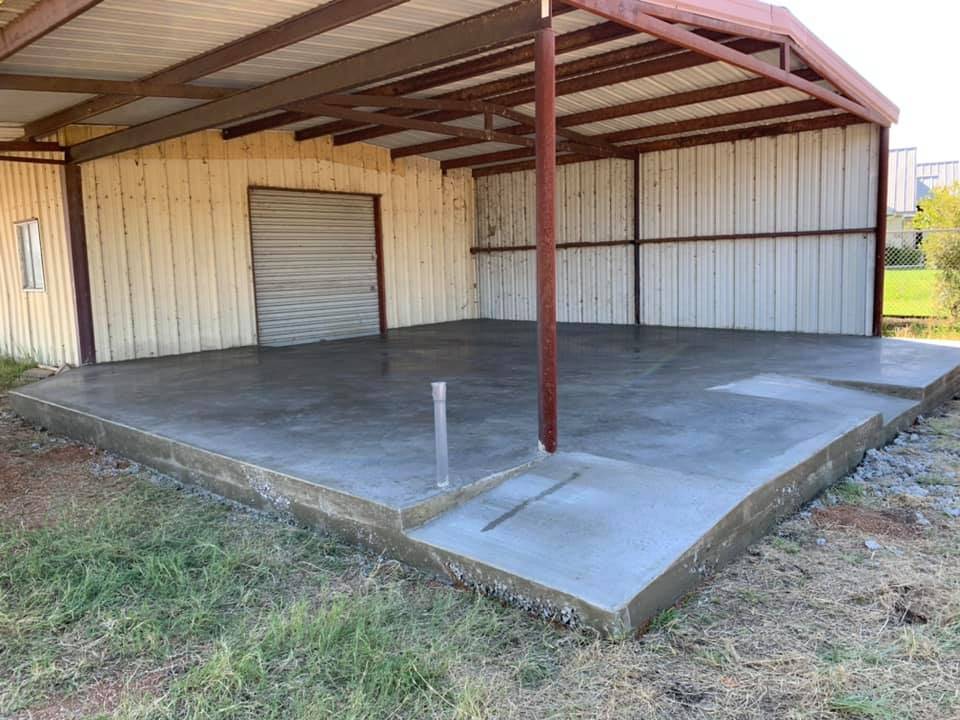 Finished concrete slab poured under a steel-frame carport and storage building
